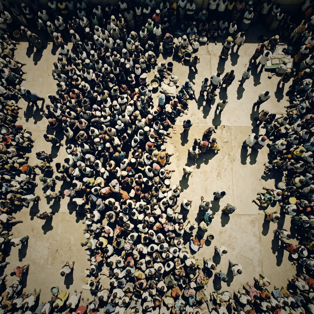 Vue plongeante sur une cour en béton occupée par une foule dense, vue du dessus, sans visage reconnaissable.
